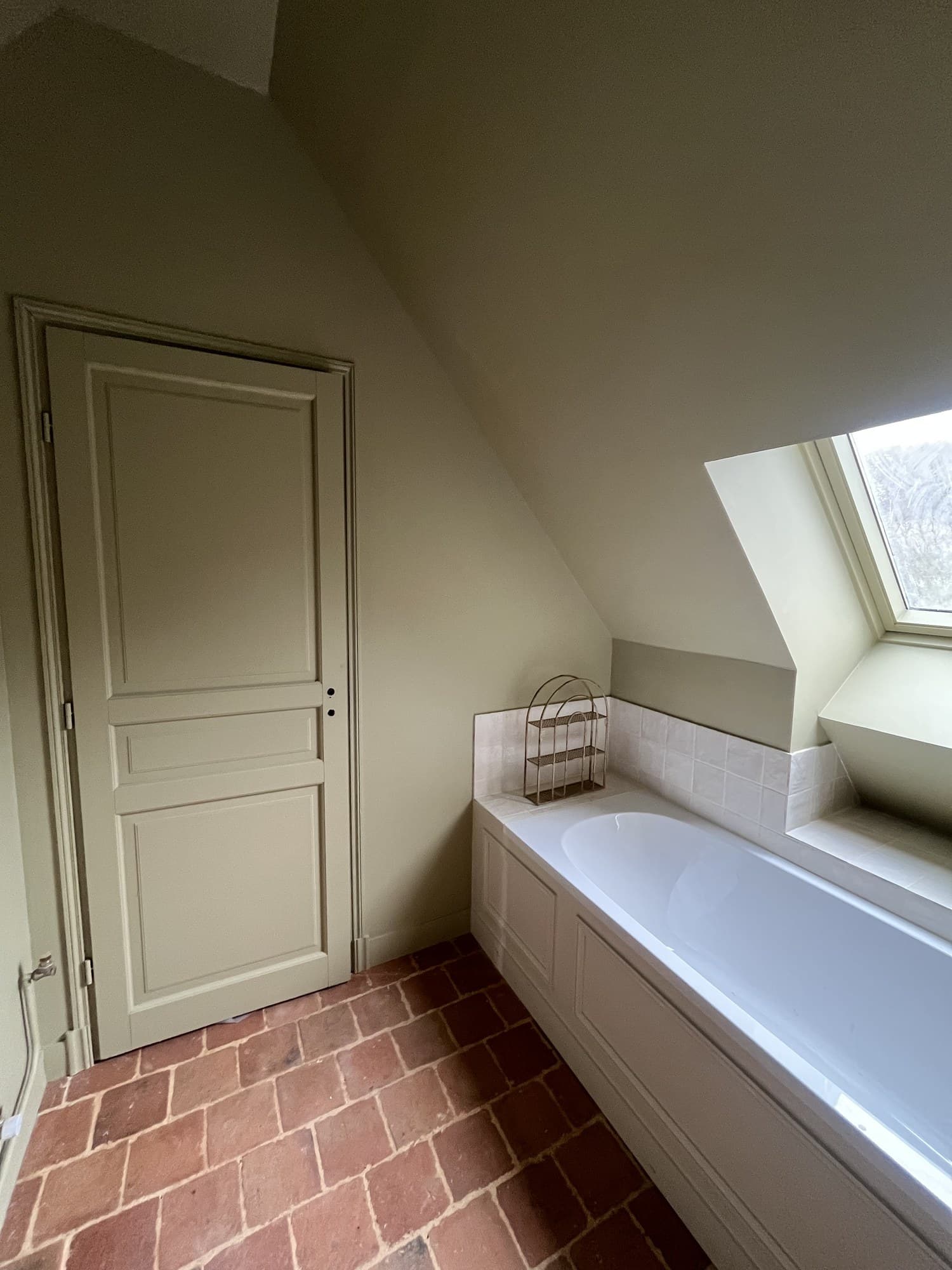 Salle de bains sous comble : baignoire encastrée, placard à panneaux peint et sol en tomettes rouges