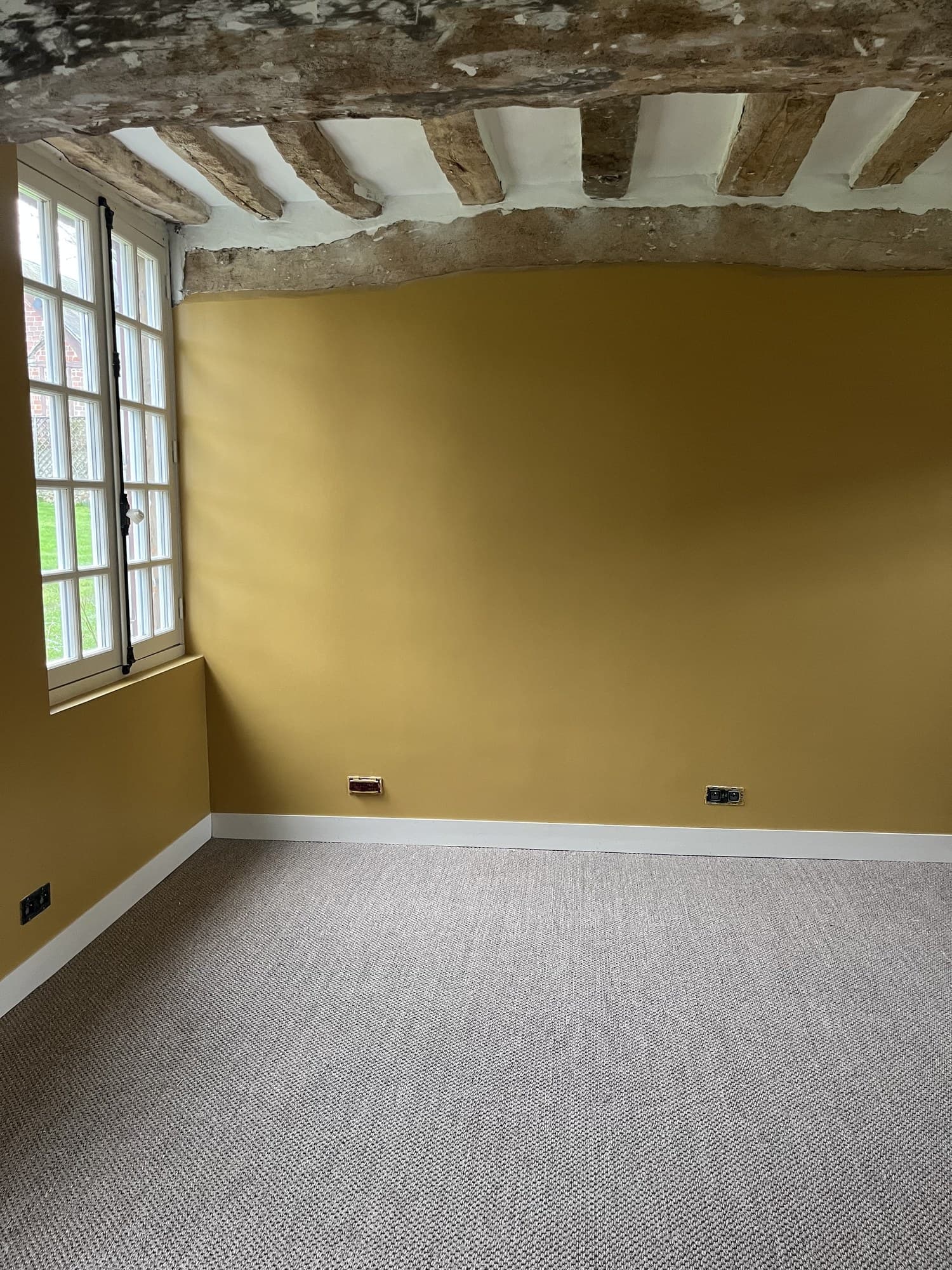 Chambre aux murs ocre profond sous un linteau de pierre et des poutres anciennes laissées nues