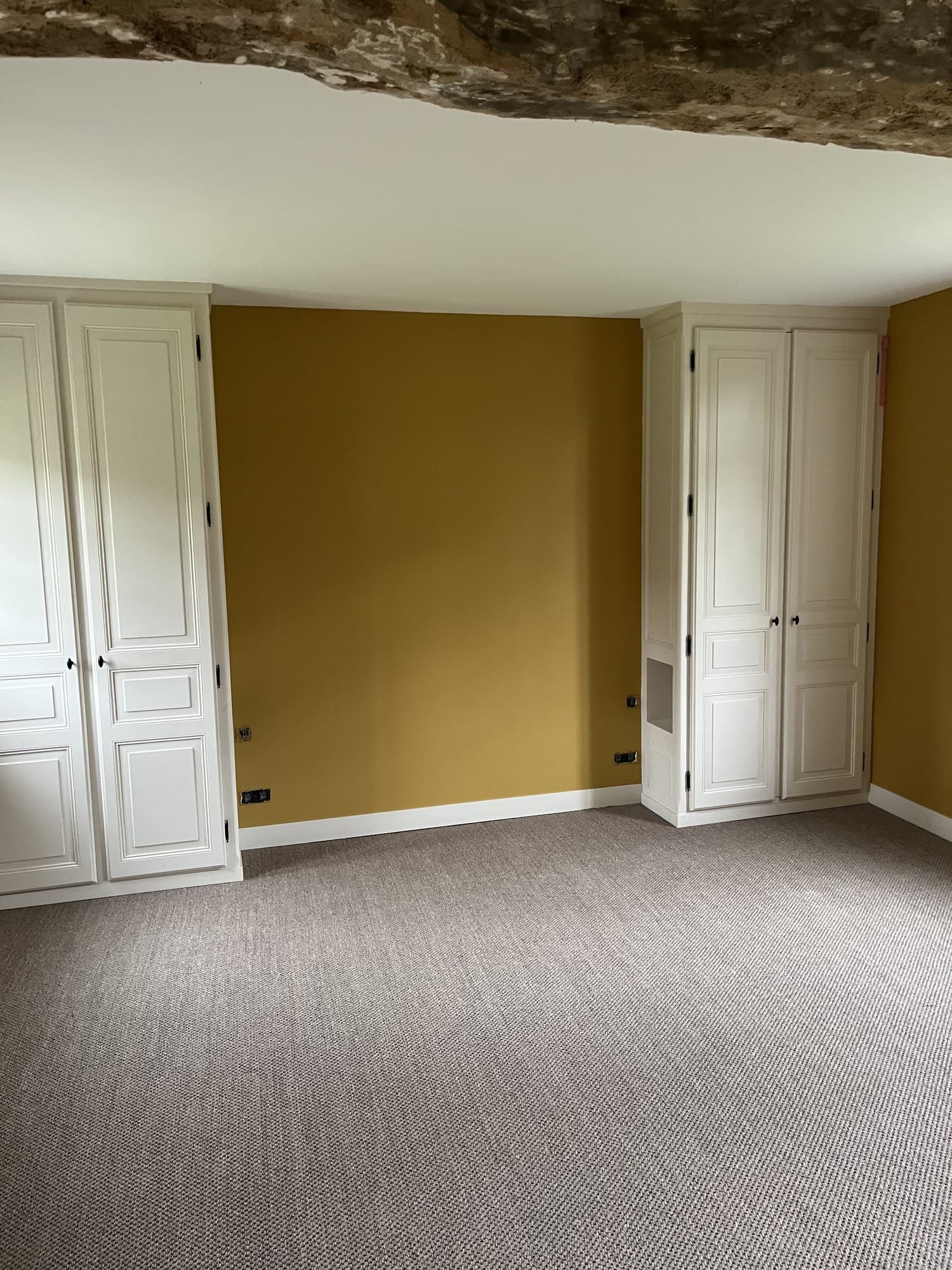 Chambre aux murs ocre, placards à panneaux moulurés peints en blanc et poutre apparente