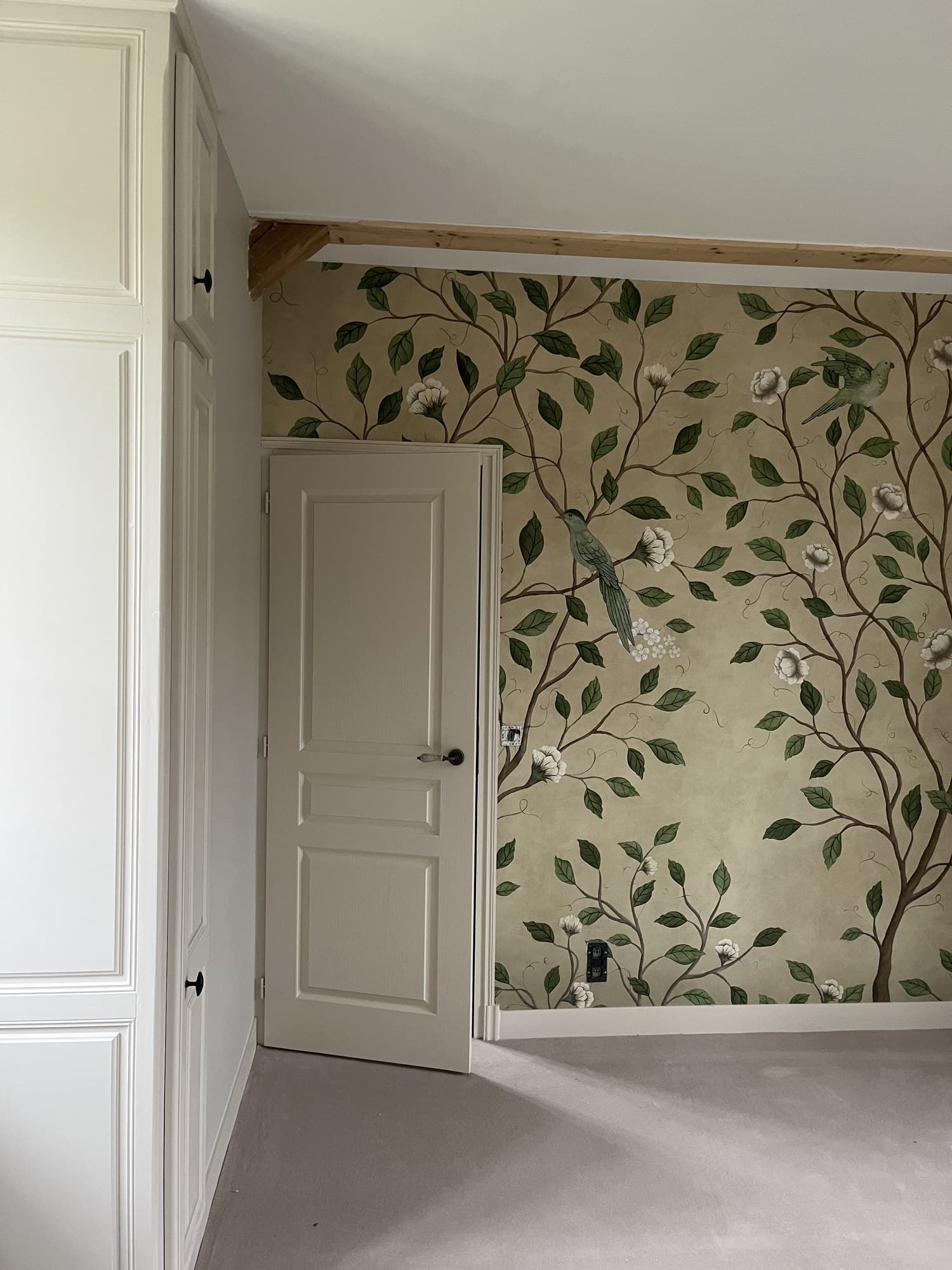Chambre aux murs à feuillages, porte moulurée peinte en blanc et poutre apparente