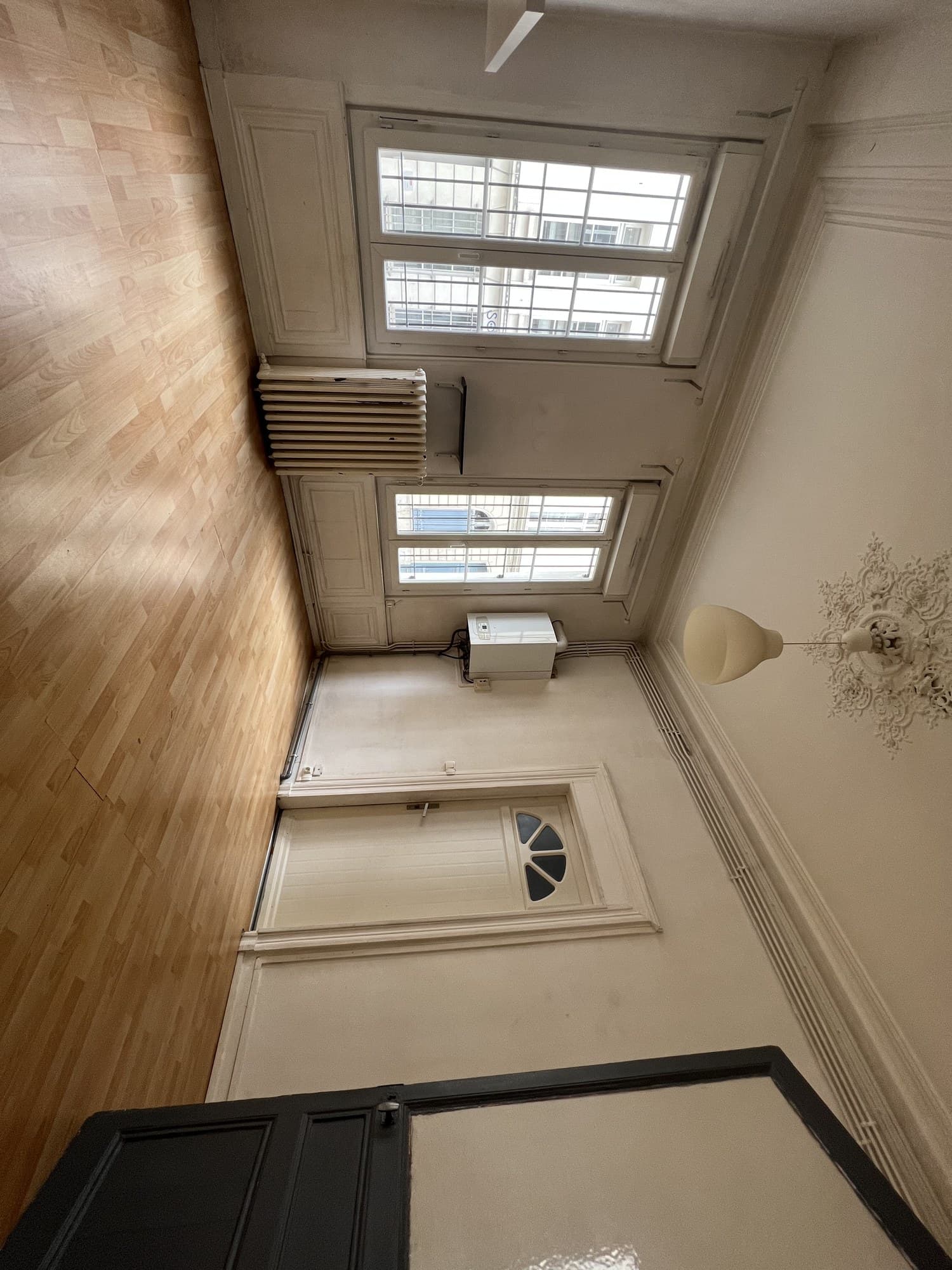 Le même séjour avant travaux, vue large : murs ternis, boiseries jaunies, radiateur fonte et gaines apparentes