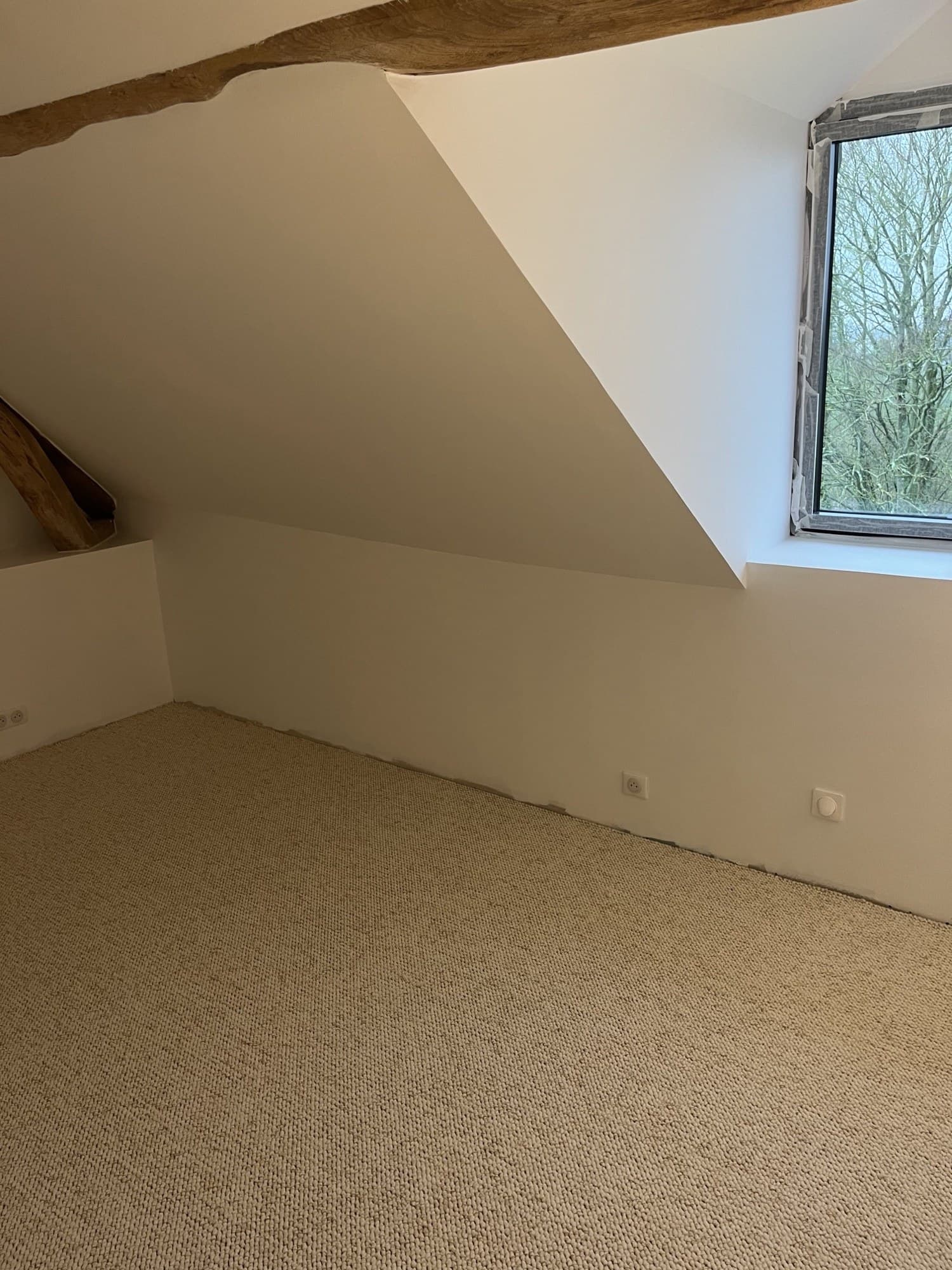 Combles terminés : murs crème mat sous charpente apparente, moquette bouclée posée
