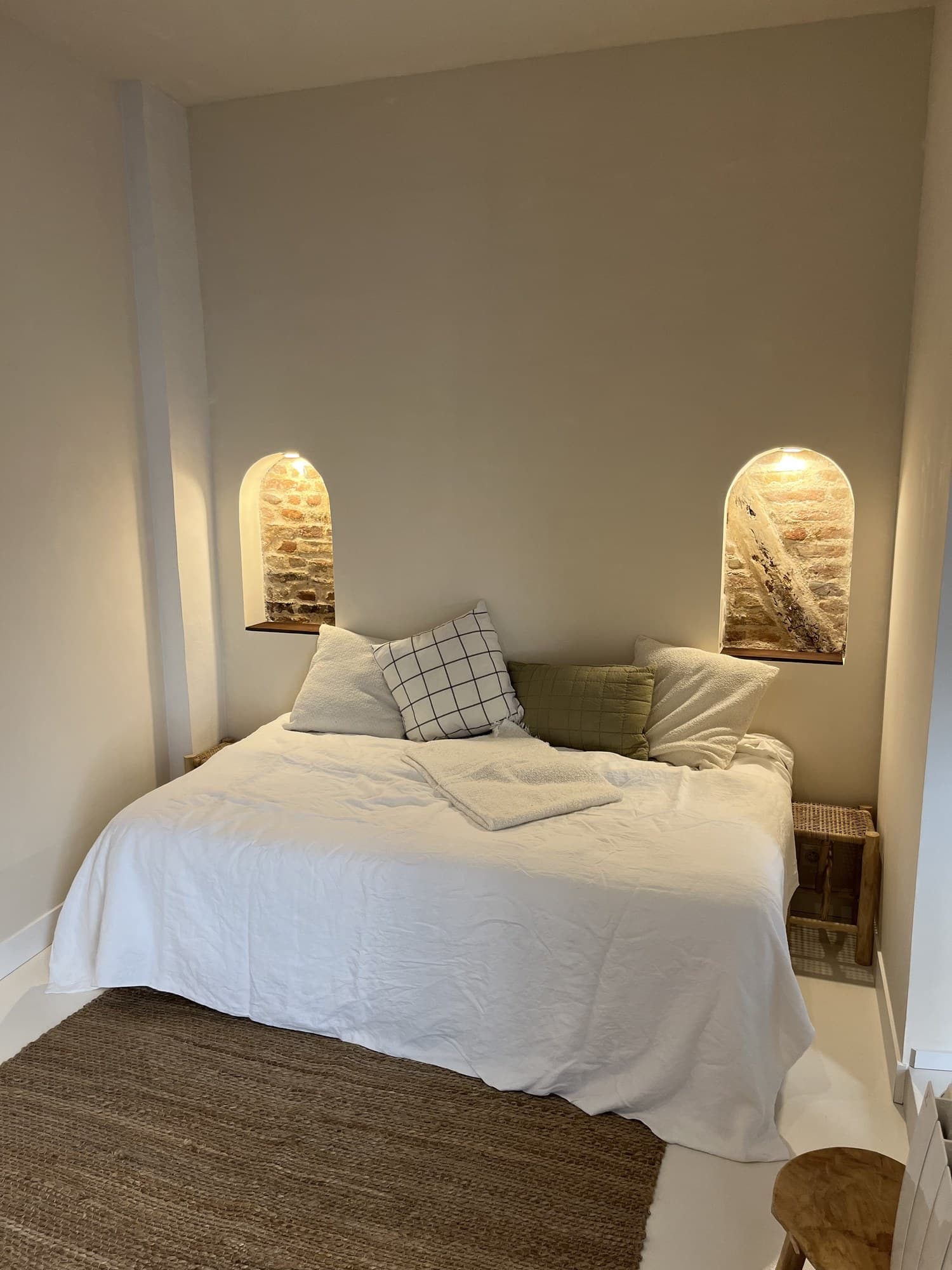 Studio meublé : lit encadré de deux niches voûtées rétroéclairées laissant voir la brique ancienne