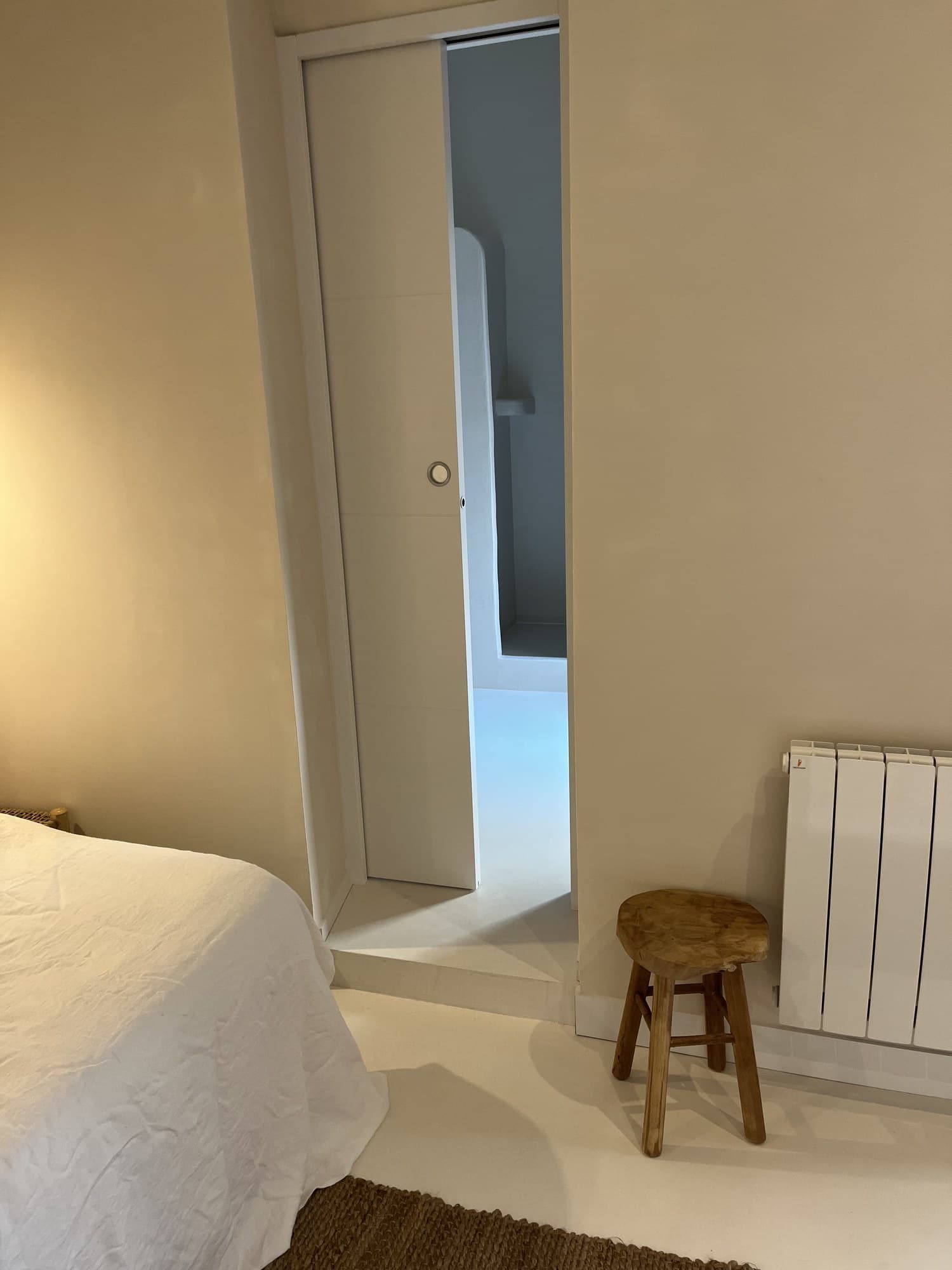 Chambre du studio : radiateur, tabouret bois et ouverture vers la salle d’eau